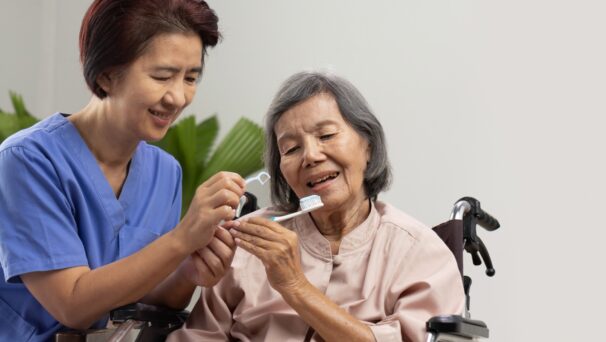 care giver helping an older lady in a wheelchair brush her teeth and maintain oral health in later life